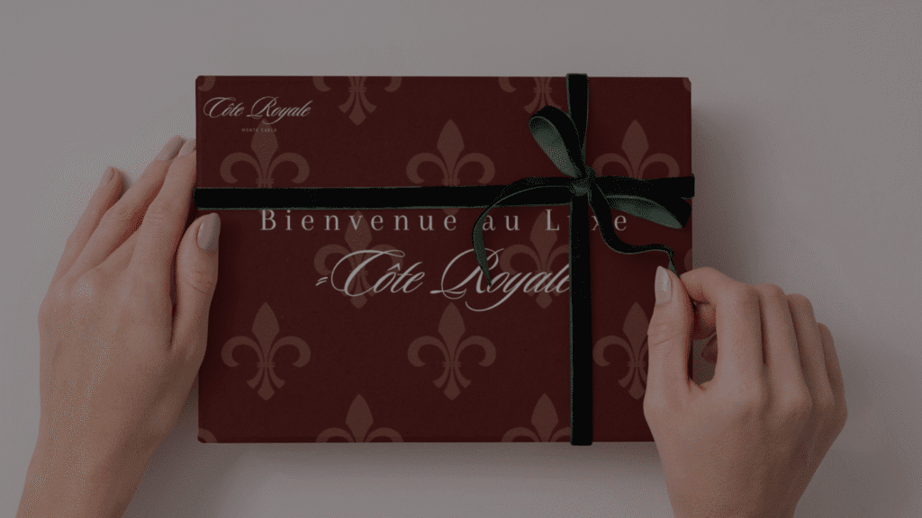 Mockup einer exklusiven Geschenkbox des Luxushotels ‚Cote Royale‘ in Monaco – schwarze Schleife, an der Frauenhände ziehen.