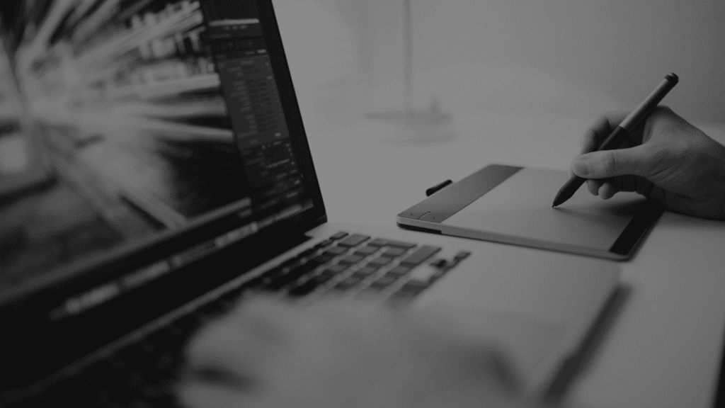 MacBook und Grafiktablet auf einem Tisch – linke Hand auf der Tastatur, rechte Hand hält einen digitalen Stift, Symbolbild für Design und Branding.