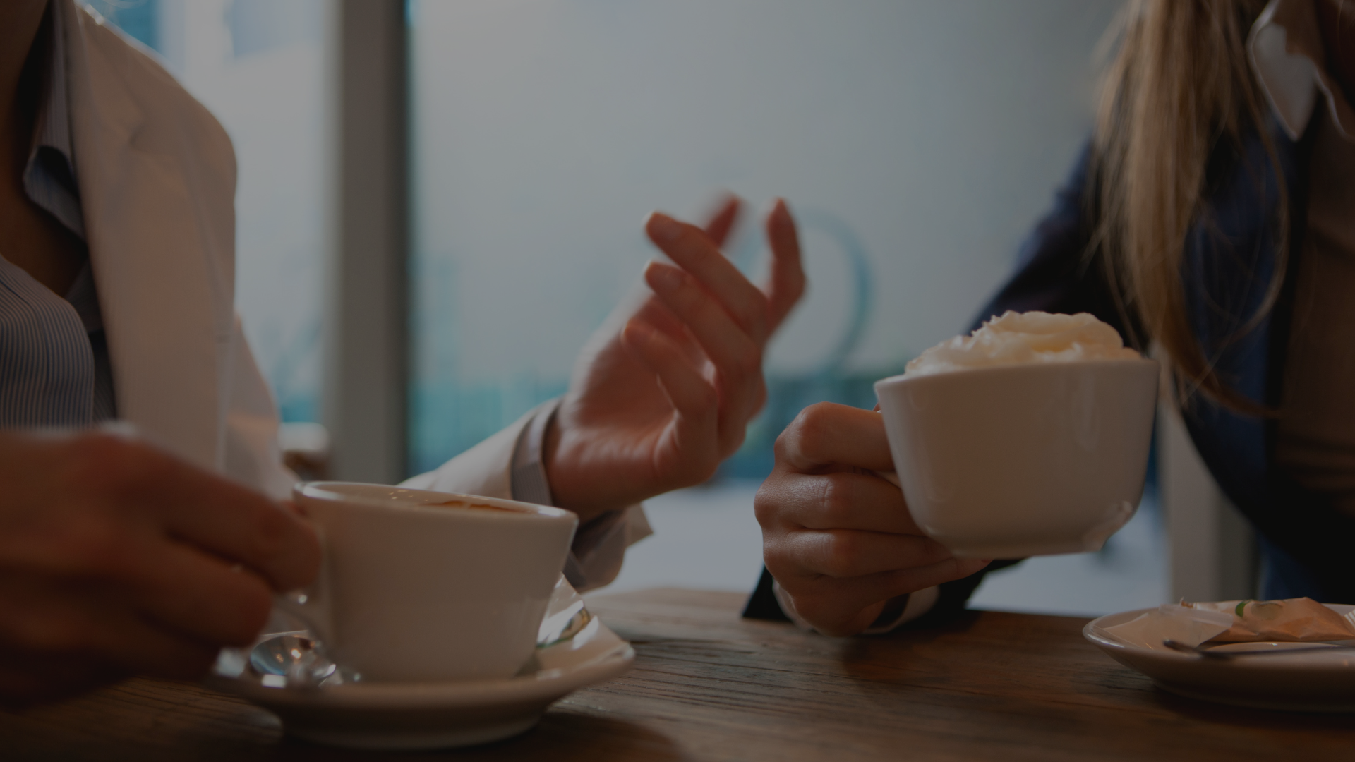 Zwei Arbeitskolleginnen unterhalten sich in der Mittagspause bei einem Cappuccino – symbolisiert Kommunikation und Austausch.