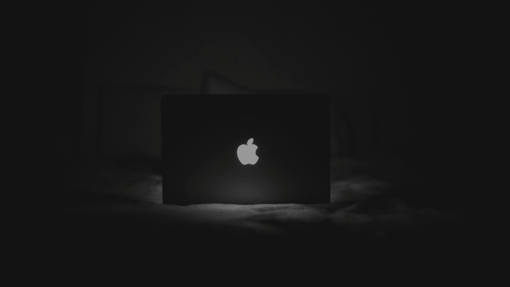 MacBook auf einem Bett mit leuchtendem Apple-Logo – symbolisiert entspanntes Arbeiten.