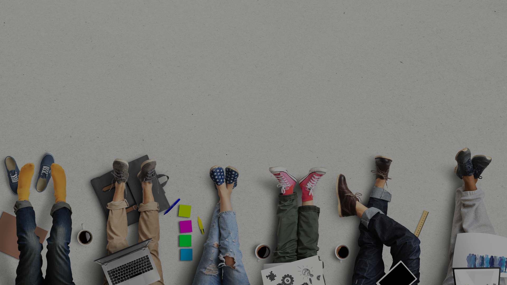 Sechs Personen aus verschiedenen Bereichen (Kreativ, Online, Büro, etc.) sitzen zusammen am Boden und arbeiten gemeinsam – symbolisiert Teamwork.